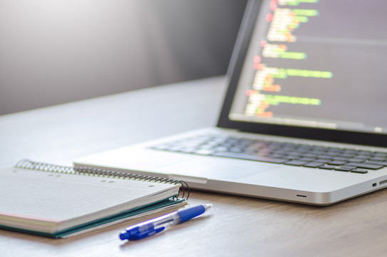 Ein Laptop, ein Notizblock und ein Kugelschreiber liegen auf einem Tisch.