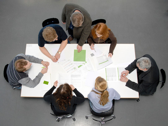 Besprechungssituation Studenten und Professoren Studierende und Dozierende sitzen gemeinsam an einem Tisch und arbeiten.