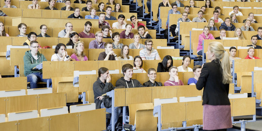 Eine Dozierende steht vor Studierenden in einem Hörsaal